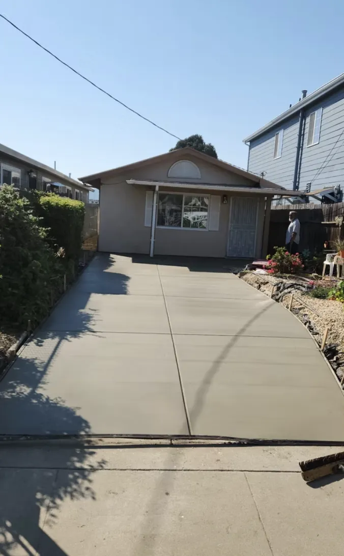 Long new concrete driveway leading up to a small house on a sunny day